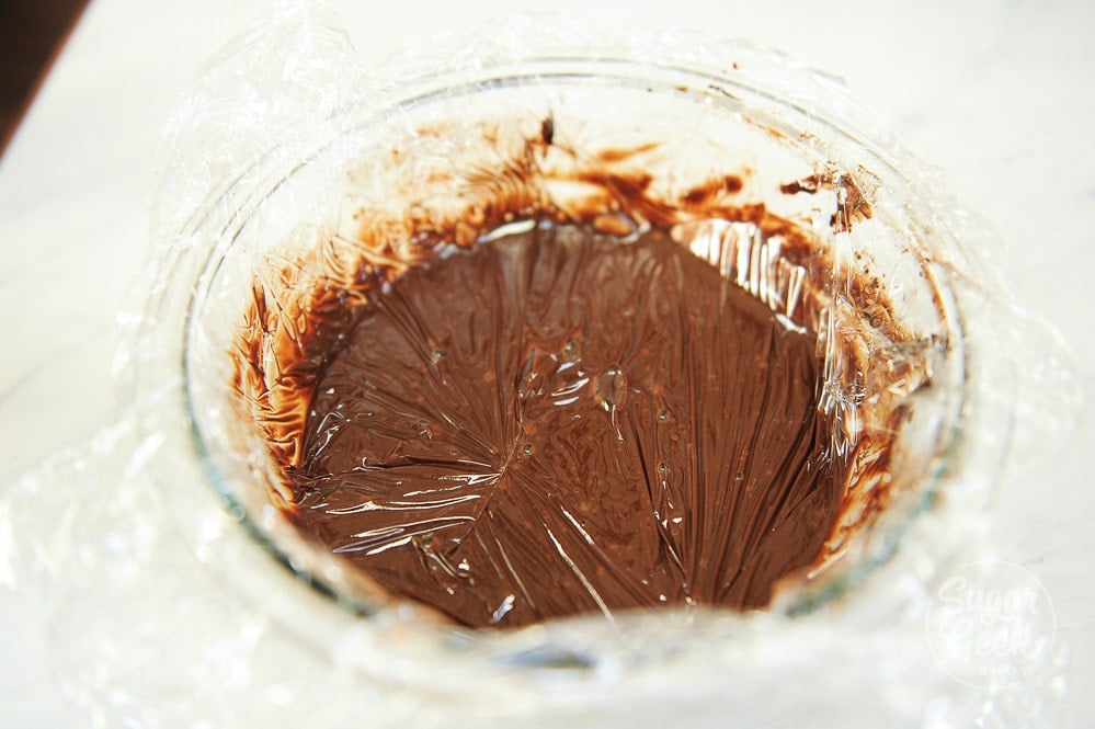 close up of a bowl of ganache with plastic wrap on top