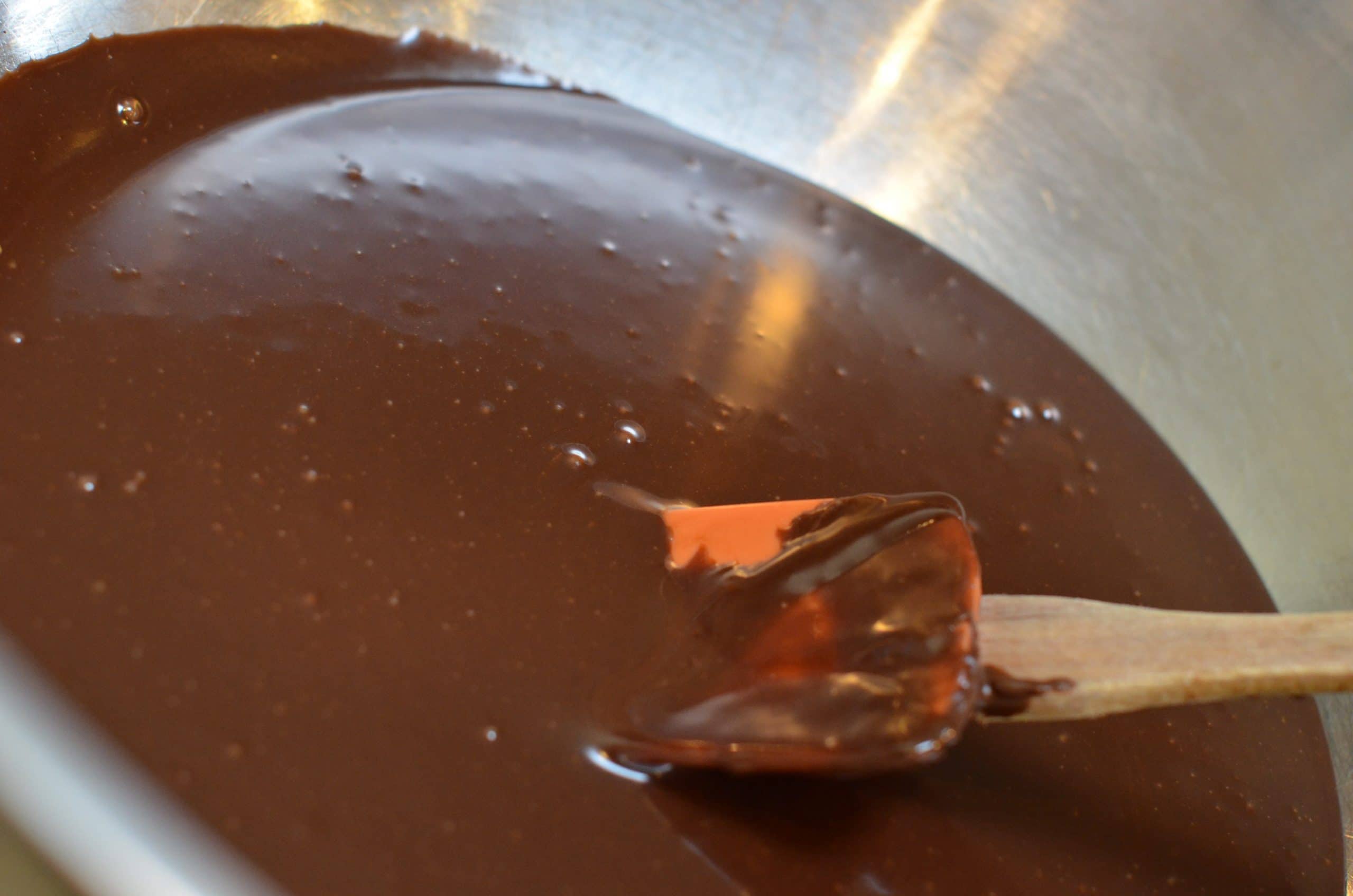Smooth melted chocolate ganache being stirred with a spatula.