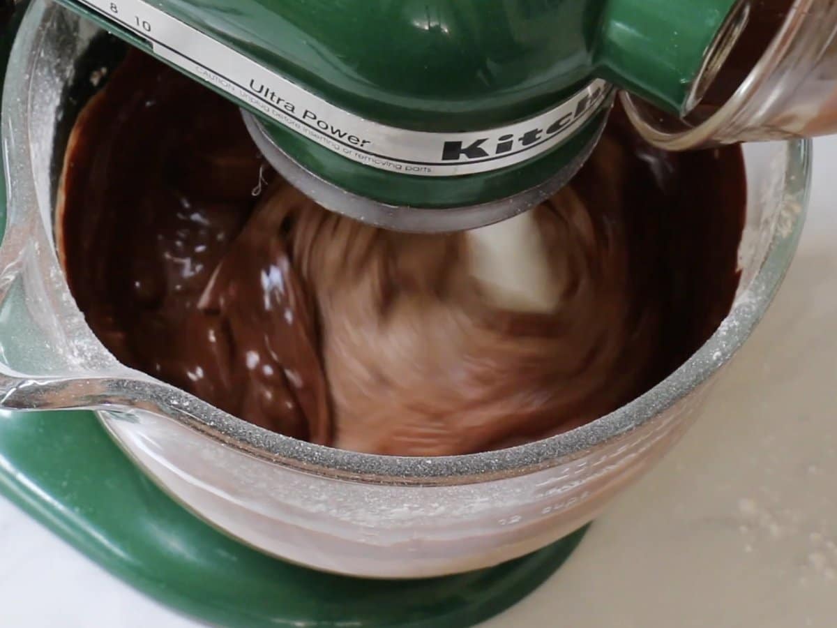 Liquid ingredients being poured into chocolate mayonnaise cake batter in a stand mixer.