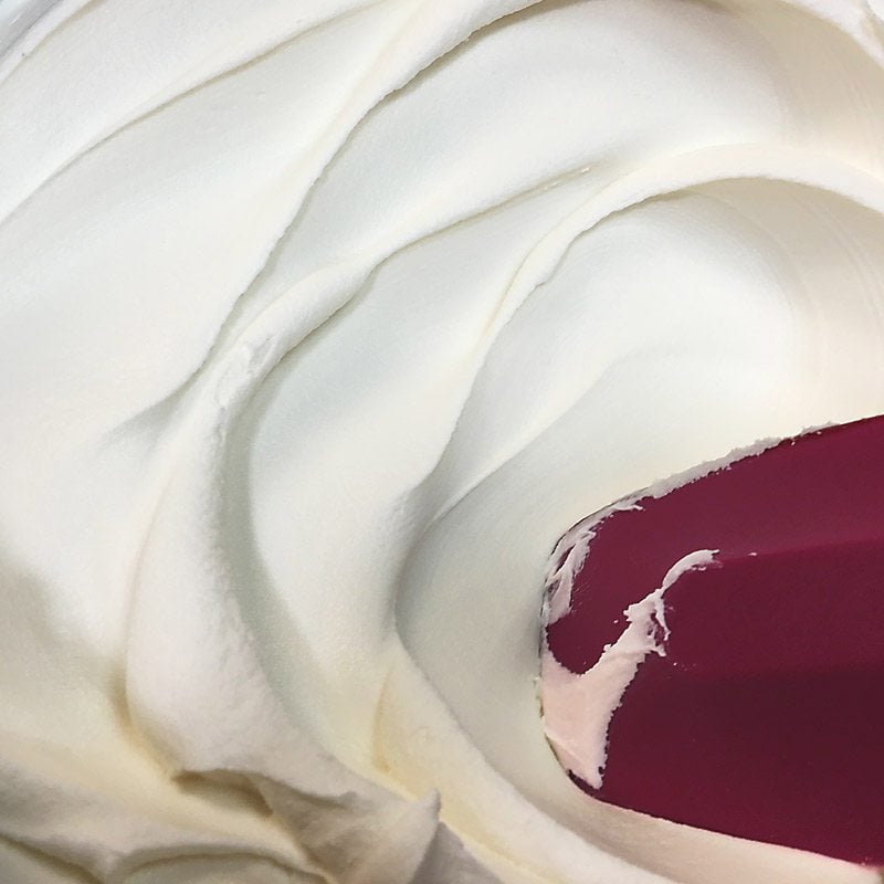 Close up of American buttercream in a bowl with a red rubber spatula.