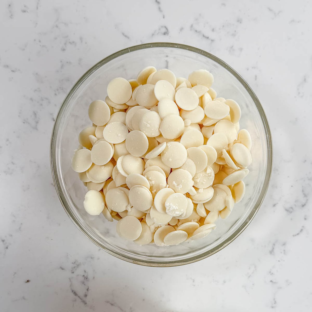 Clear glass bowl with white chocolate inside.