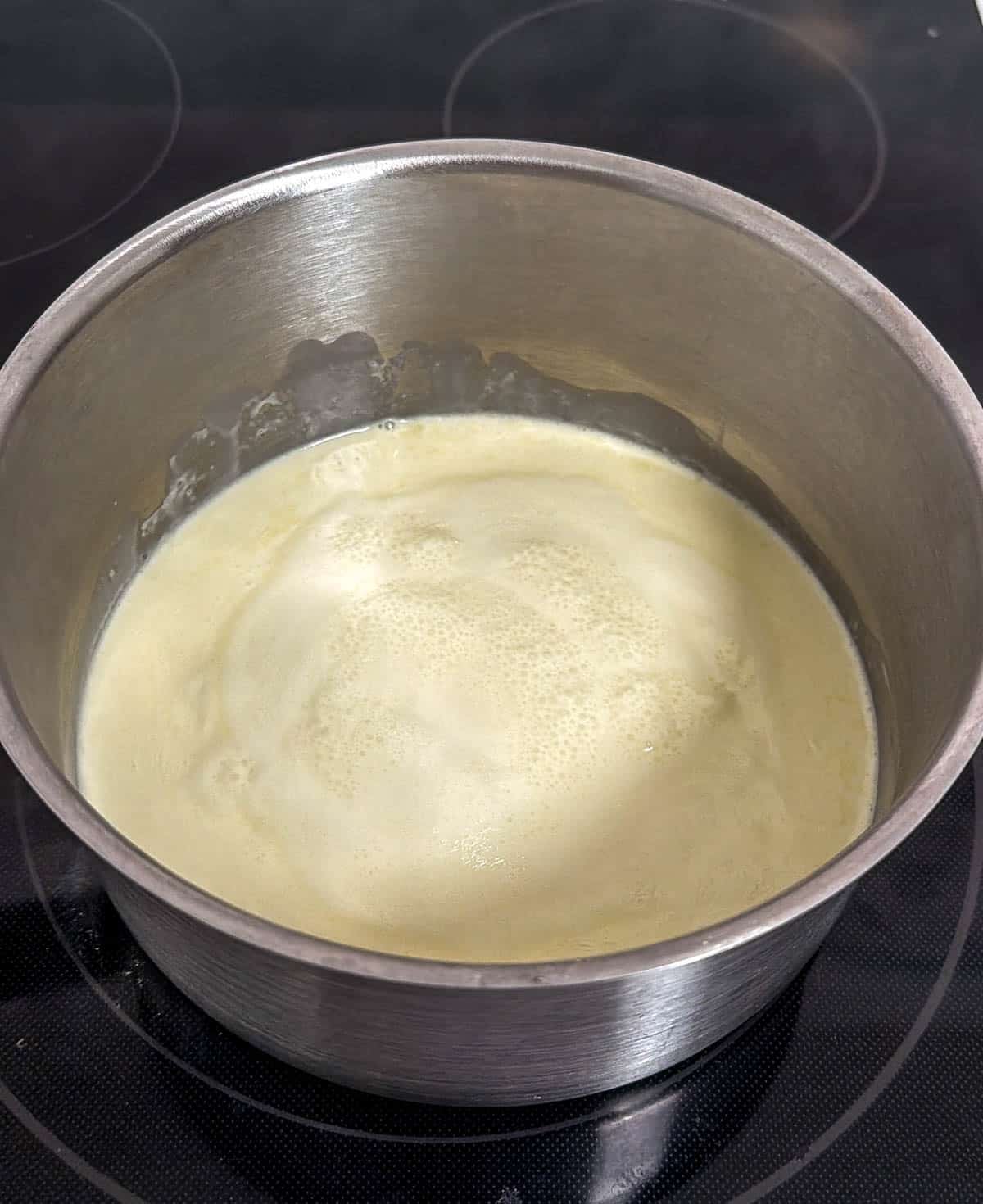 Metal saucepan with heavy whipping cream bubbling inside.