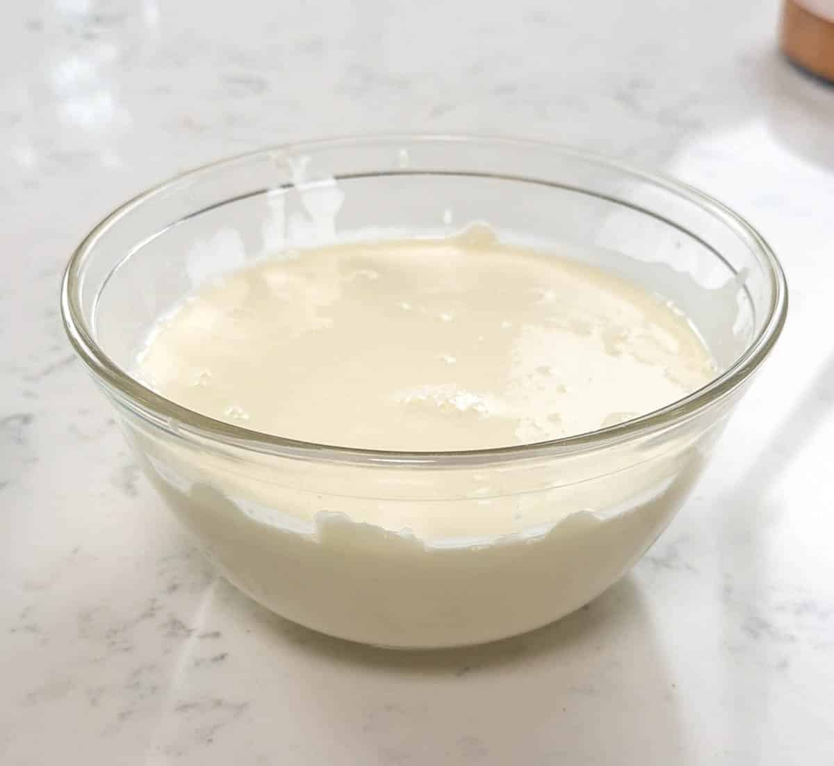 Close up of white chocolate ganache in a clear glass bowl.