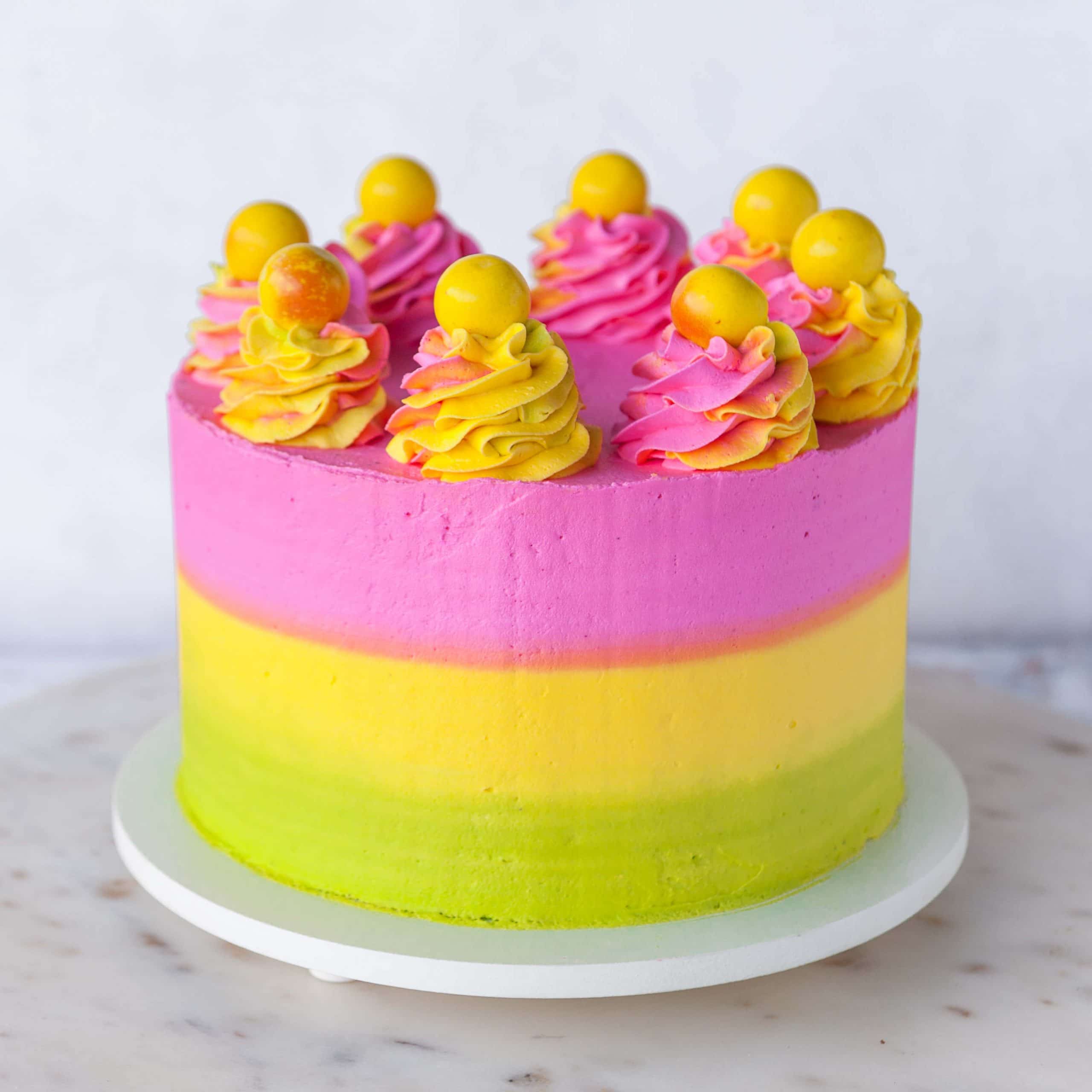 neon pink, yellow and green striped buttercream cake with swirls of buttercream on top and bright yellow gumballs