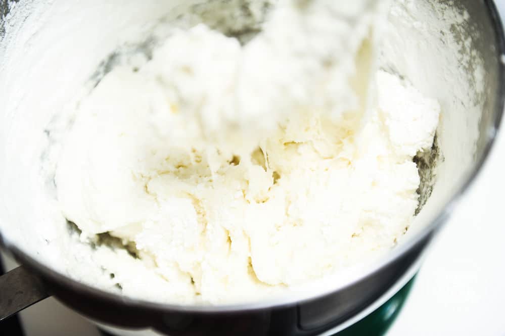 Close up of marshmallows mixing in a stand mixer bowl with a hook attachment.