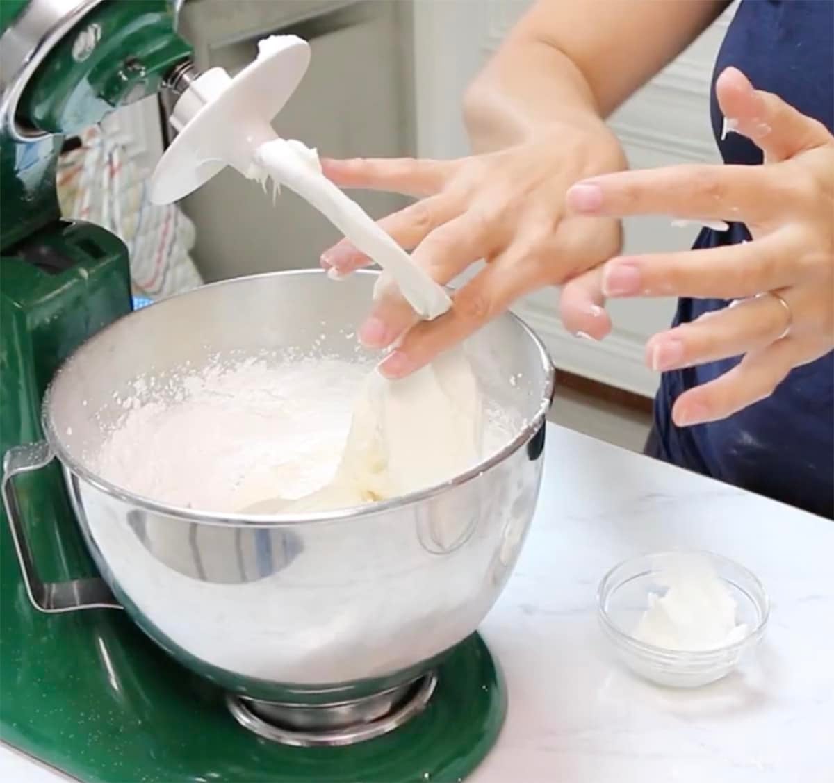 Hands removing fondant mixture from the hook attachment of a stand mixer with vegetable shortening