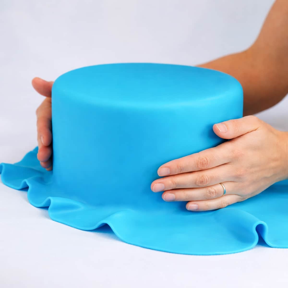 Hands wrapped around a cake covered in blue fondant.