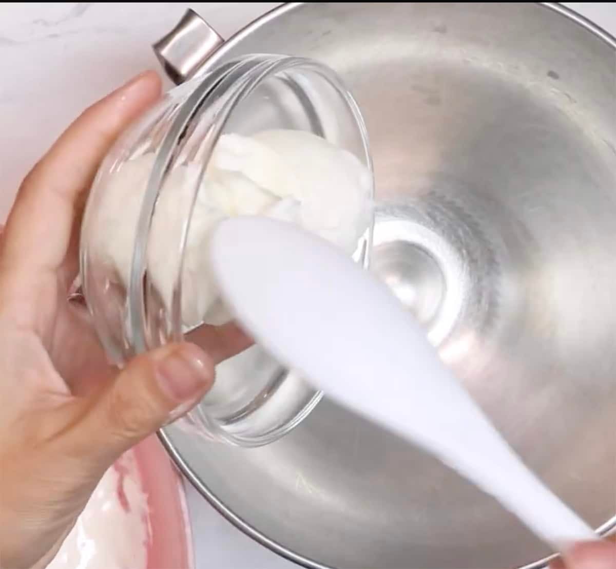 White spoon placing vegetable shortening from a small clear bowl into a metal stand mixer bowl.