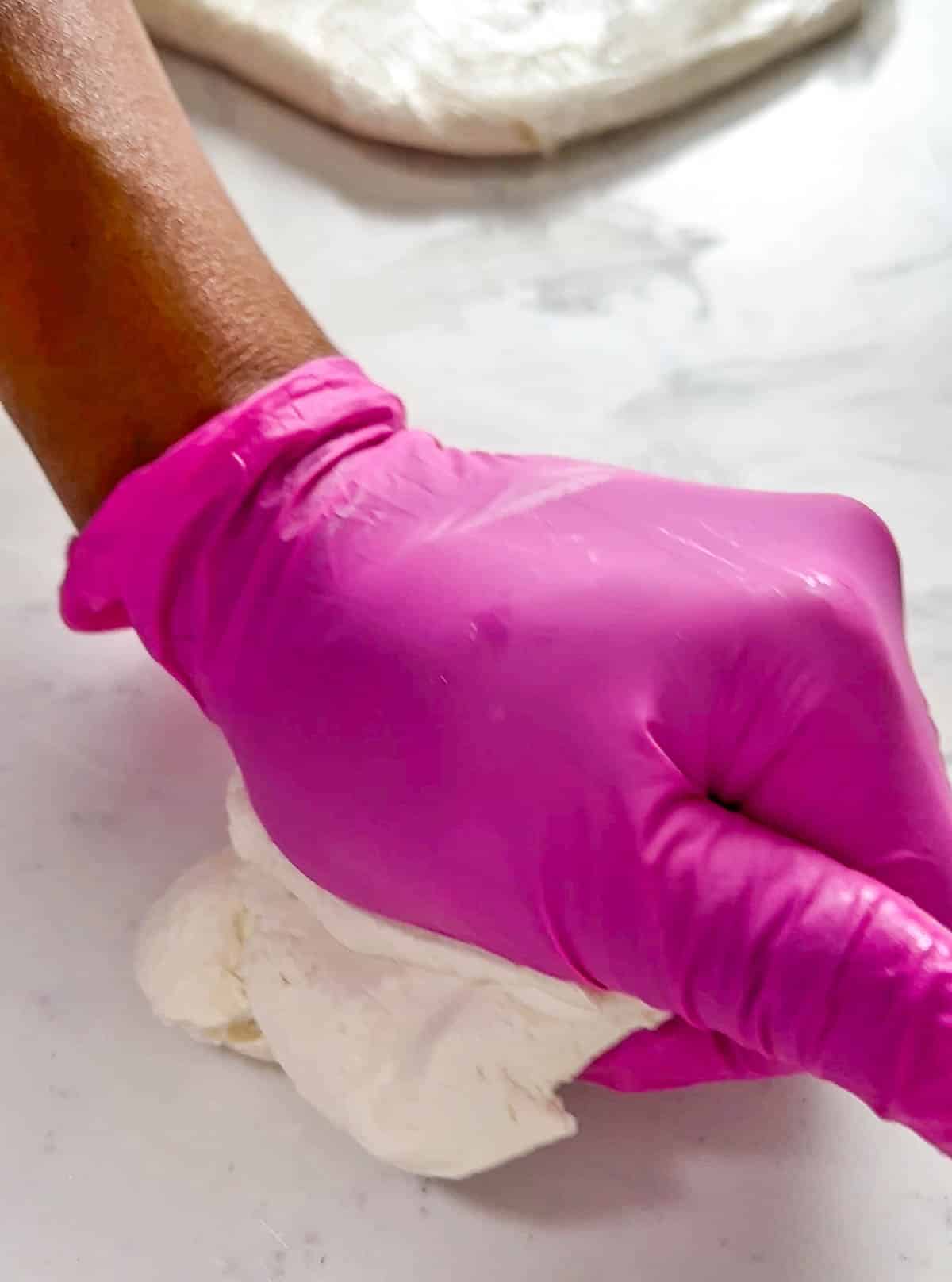 Pink gloved hand kneading modeling chocolate.