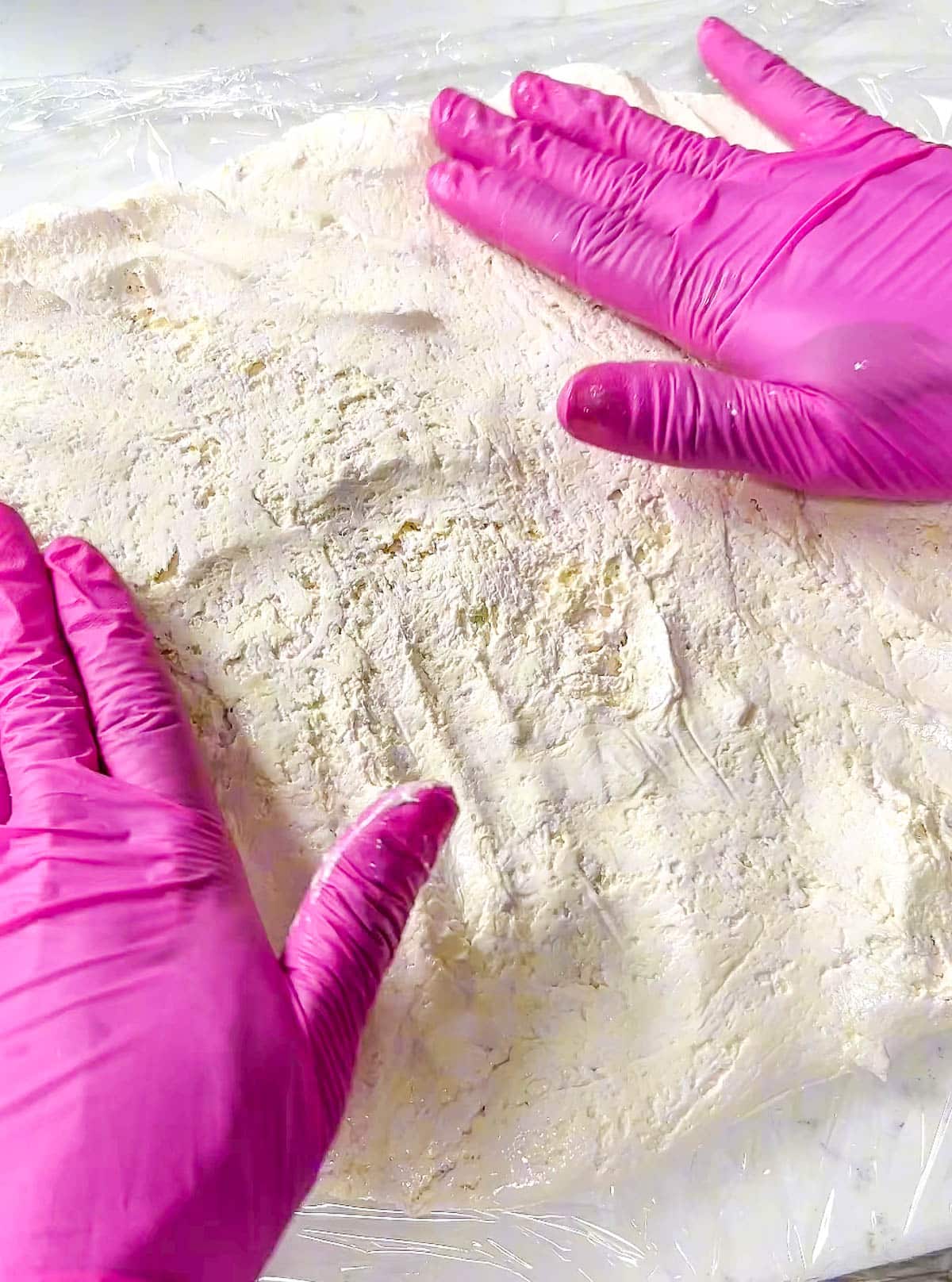 Hand with pink gloves pressing modeling chocolate flat.