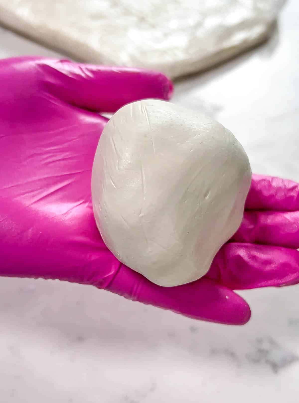 Pink gloved hand holding a round ball of modeling chocolate.