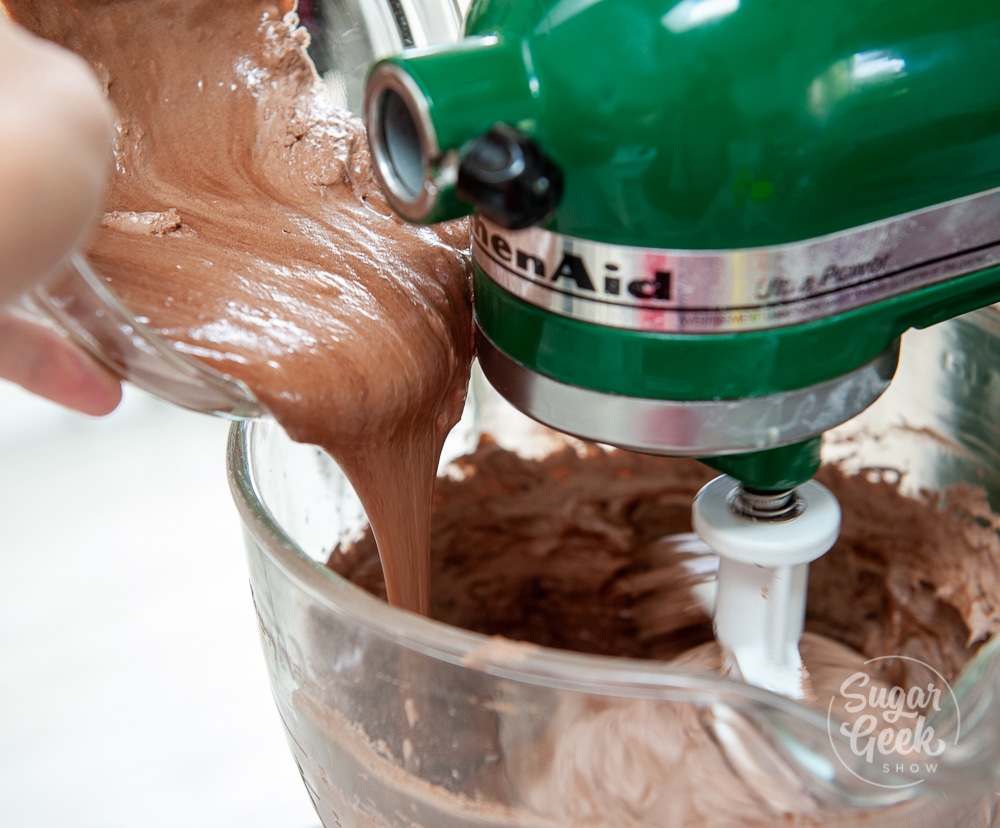 pouring melted buttercream into the bowl of a stand mixer