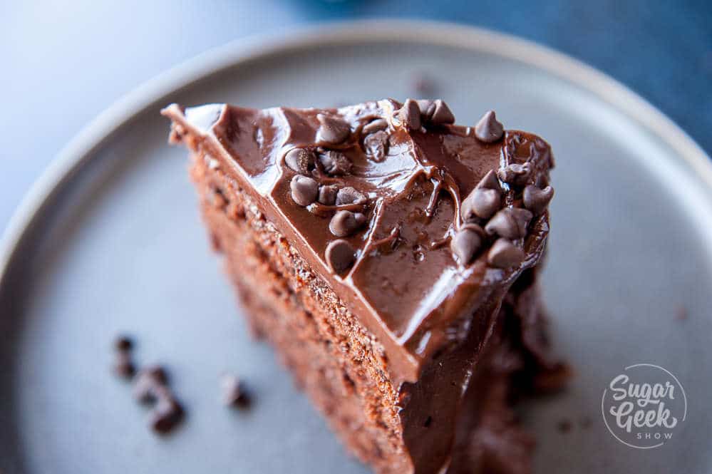 närbild på en skiva chokladkaka med chokladglasyr och chokladbitar på toppen