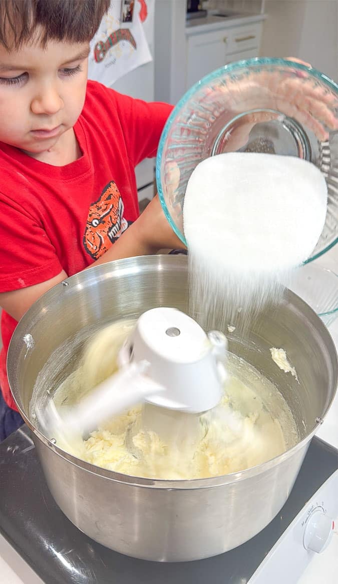 small boy adding a bowl of sugar to funfetti cake ingredients