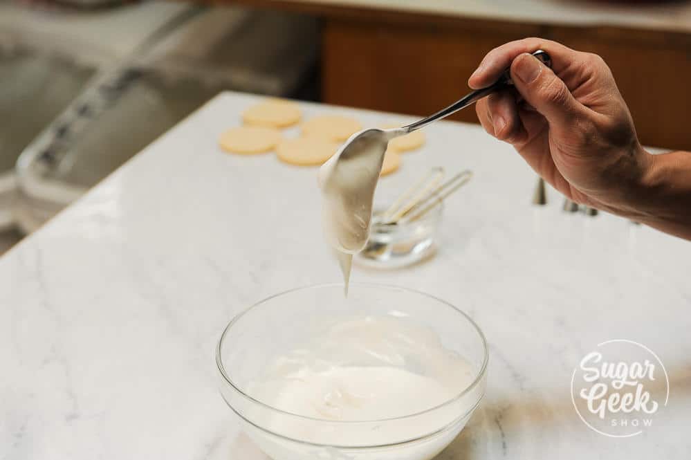 Thick, stiff royal icing on a spoon over a glass bowl.