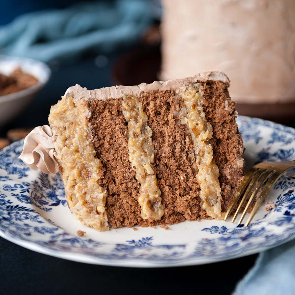 close up of german chocolate cake on a blue patterned plate with cake in the background