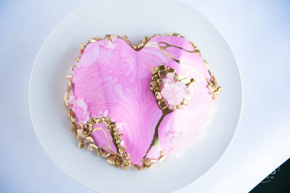 Geometric heart entremet cake with pink marbled mirror glaze and sugar crystals.