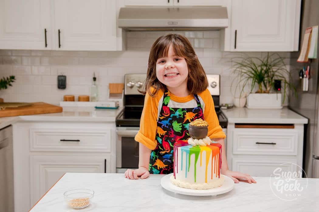 kid baking rainbow drip pot of gold cake for saint patricks day