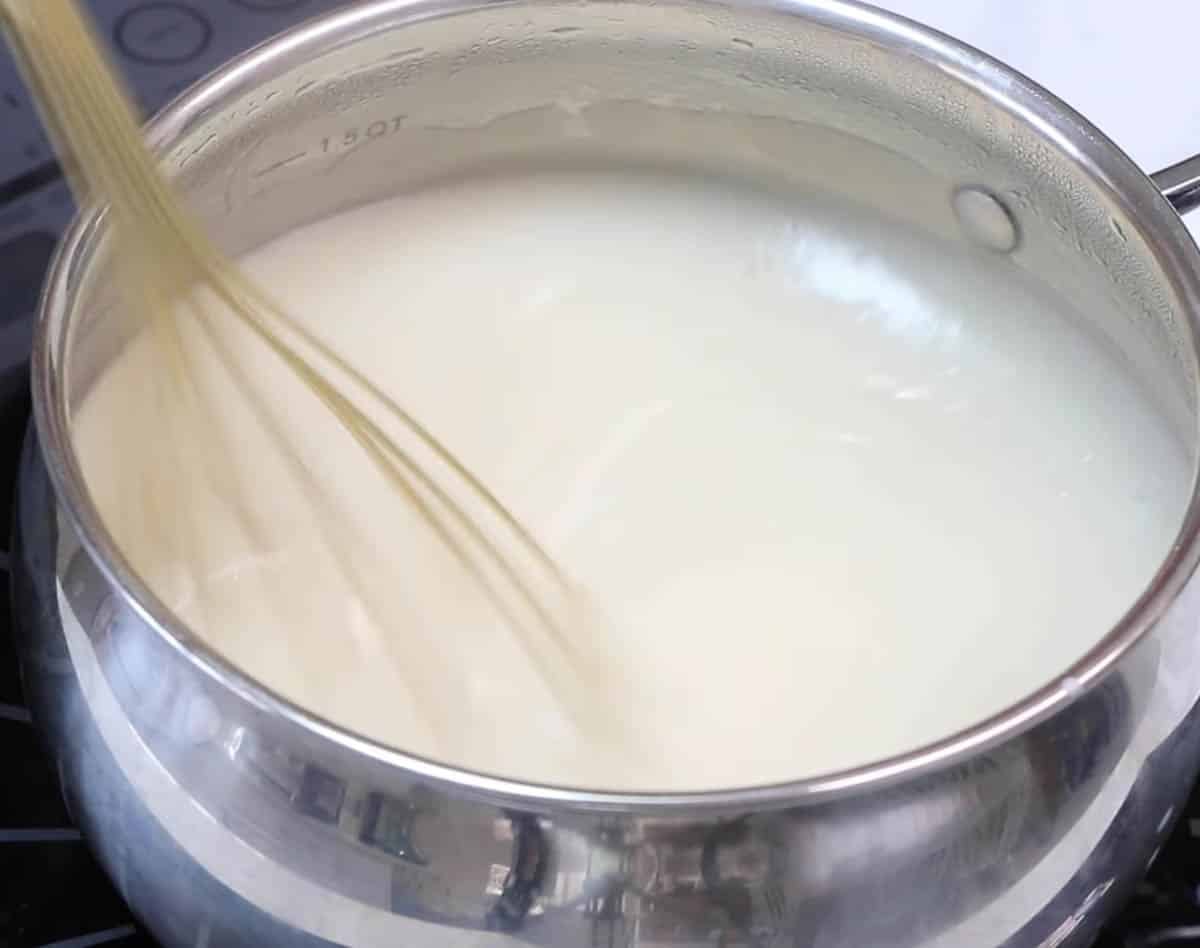 Ermine frosting mixture with a gold whisk inside a metal saucepan.