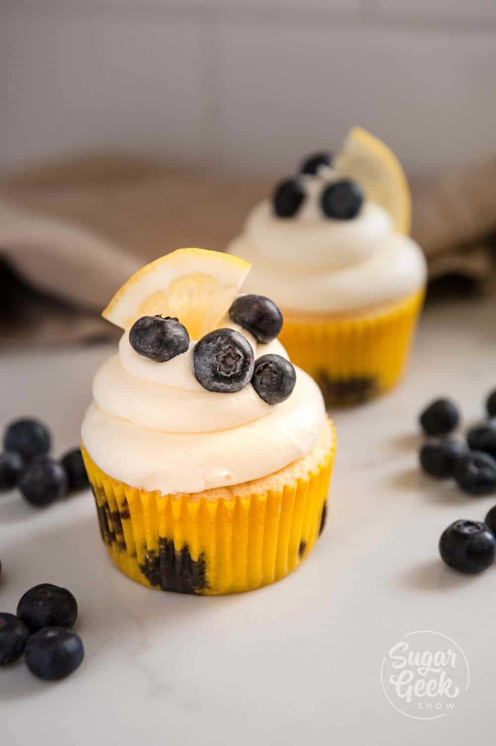 lemon blueberry cupcakes with cream cheese frosting and topped with fresh blueberries and a lemon slice