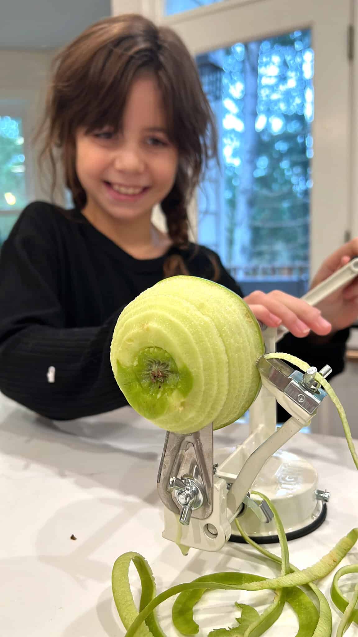 Smiling little girl peeling apples with an apple peeler.