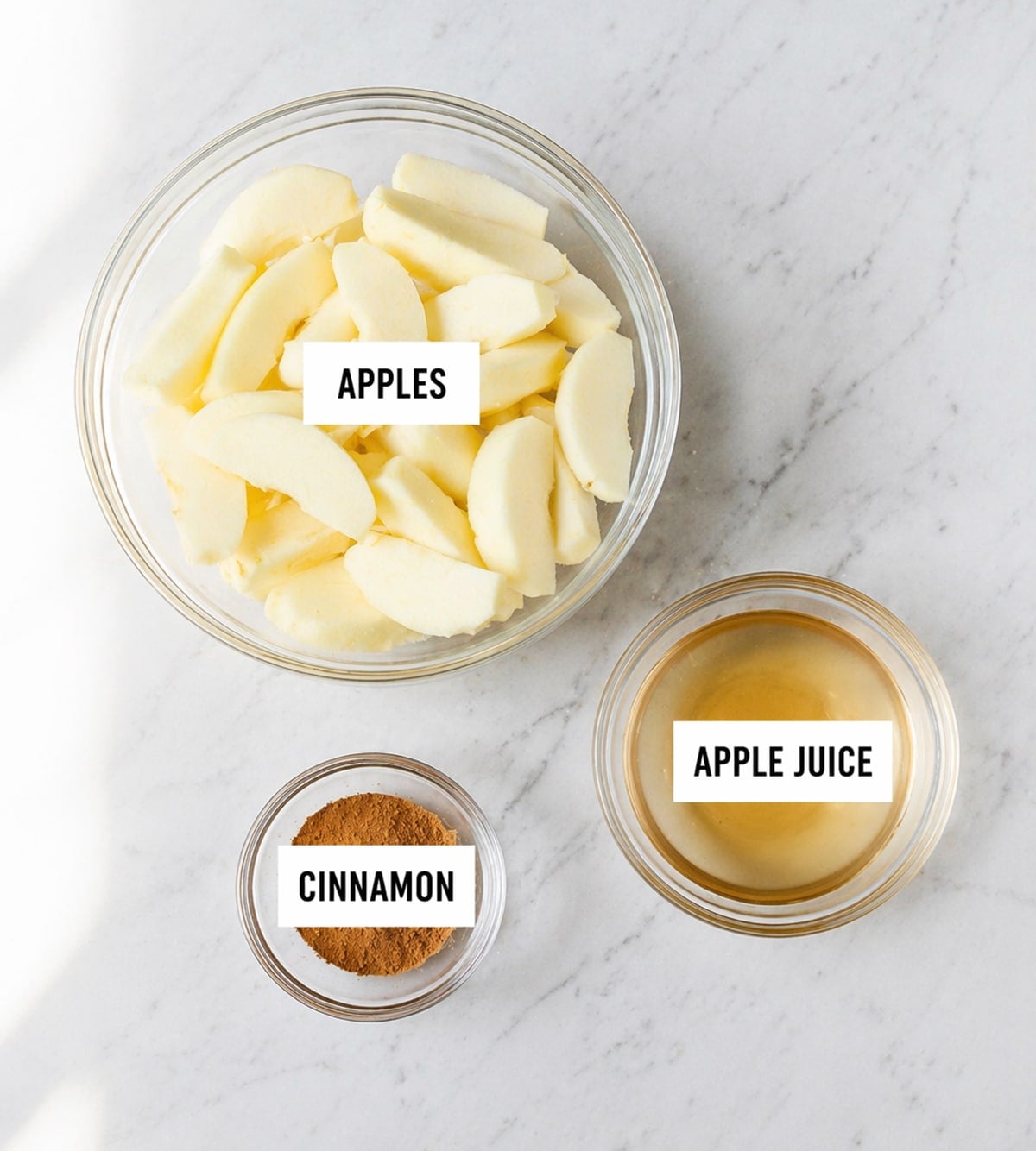 Applesauce ingredients in clear bowls on a white countertop.