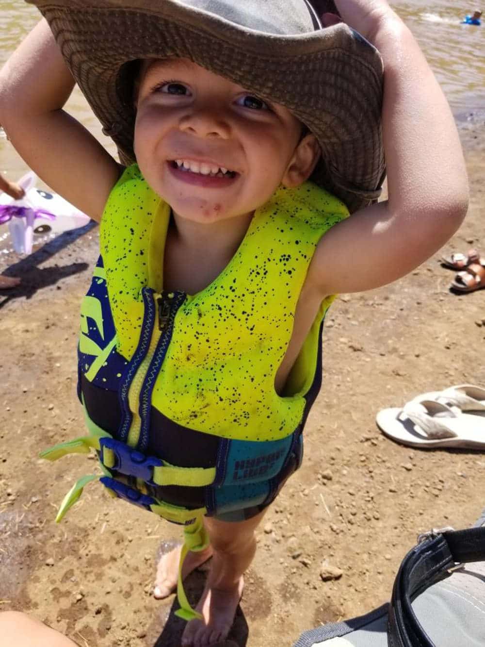 little boy wearing life jacket and hat at the lake
