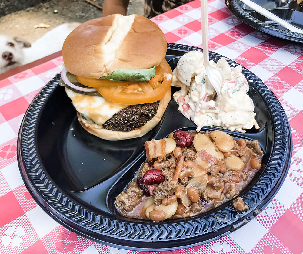 Grilled burger, potato salad and baked bean casserole on a black plate