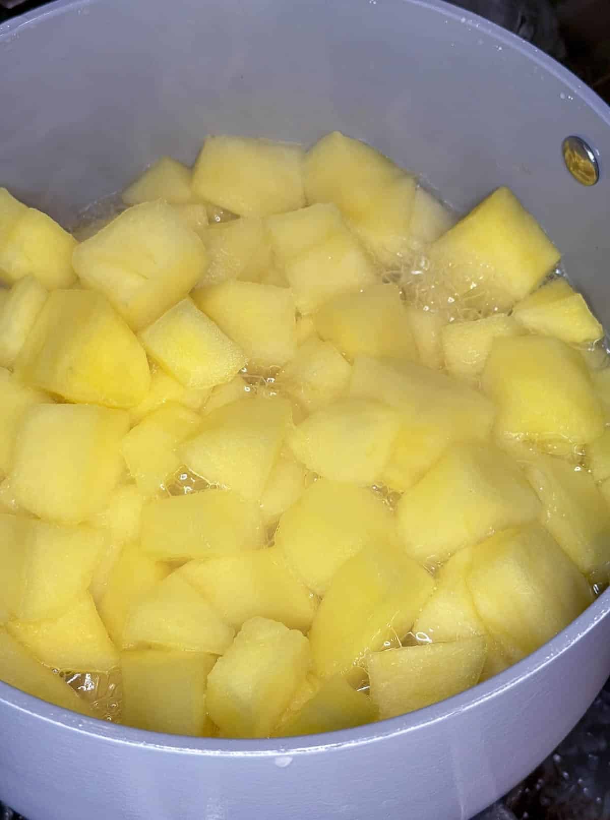 Cubed apples simmering in a grey and white saucepan.