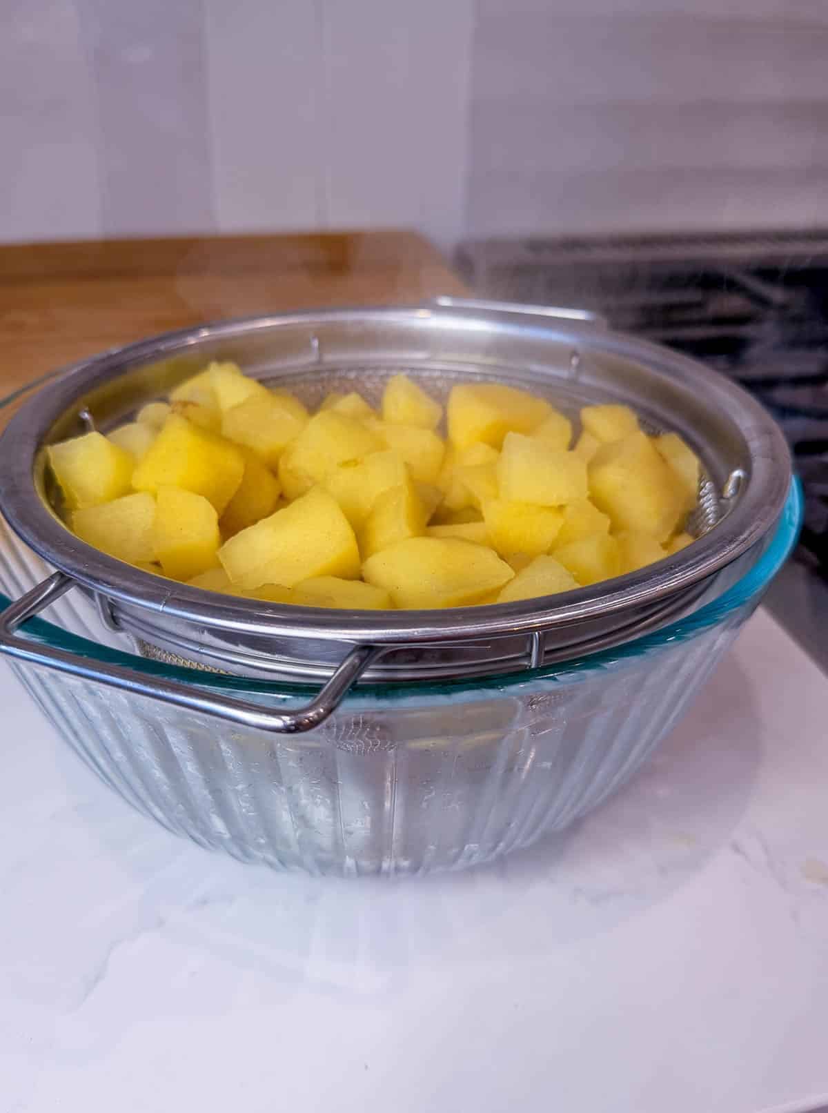 Cooked apples in a strainer over a glass bowl.