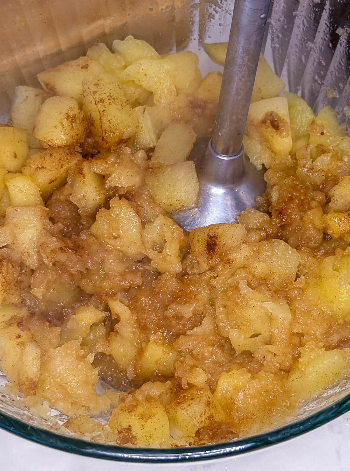 Immersion blender blending apples with cinnamon in a clear bowl.