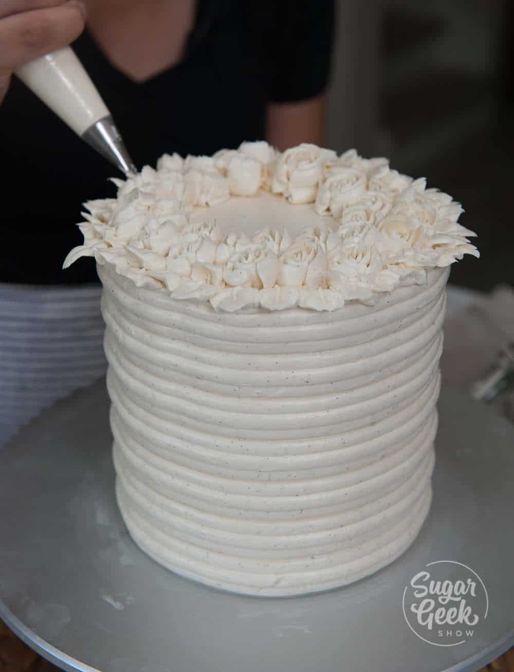 piping buttercream leaves next to buttercream roses on top of the finished cake