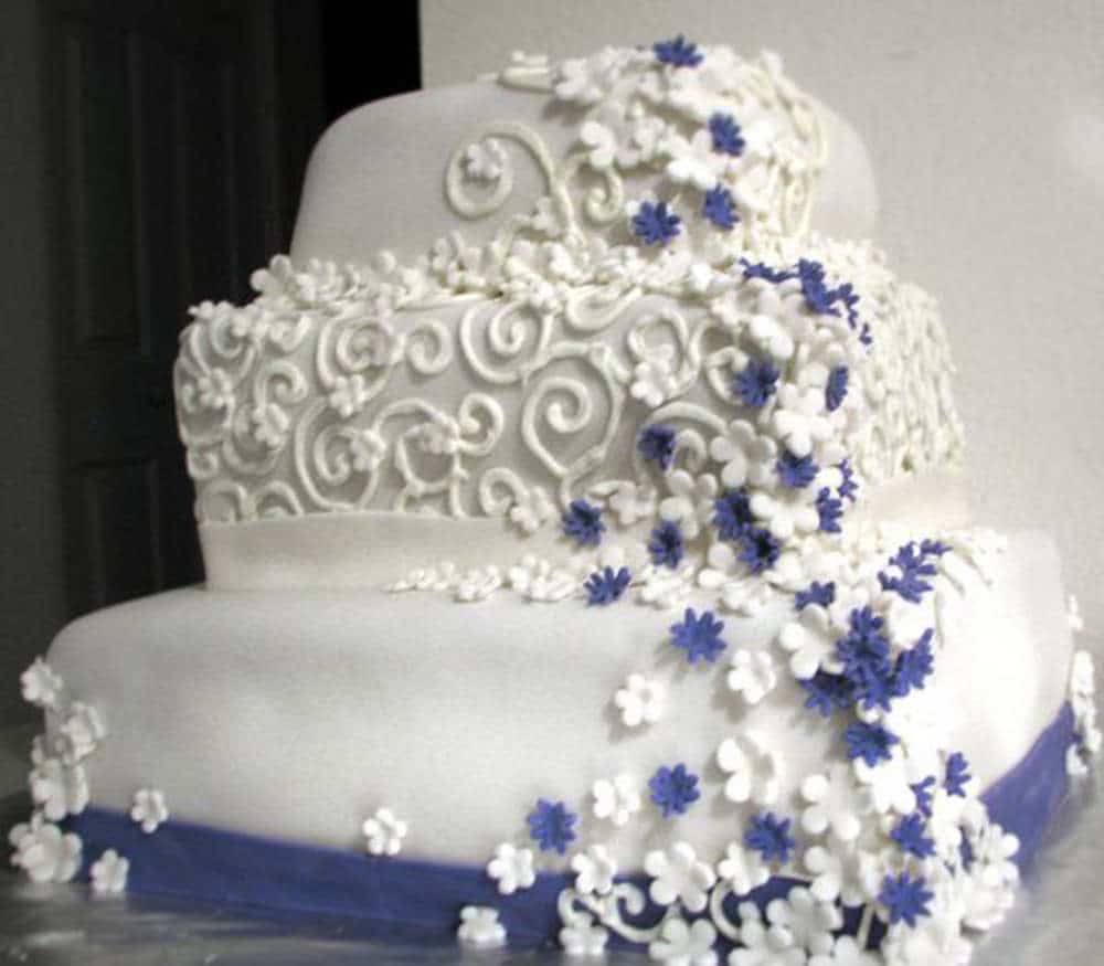 Three tier white wedding cake with crooked sides and corners. Bad piping and ugly fondant flowers