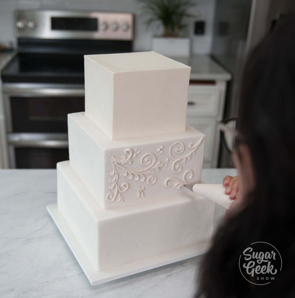 Woman decorating a three tier square wedding cake.