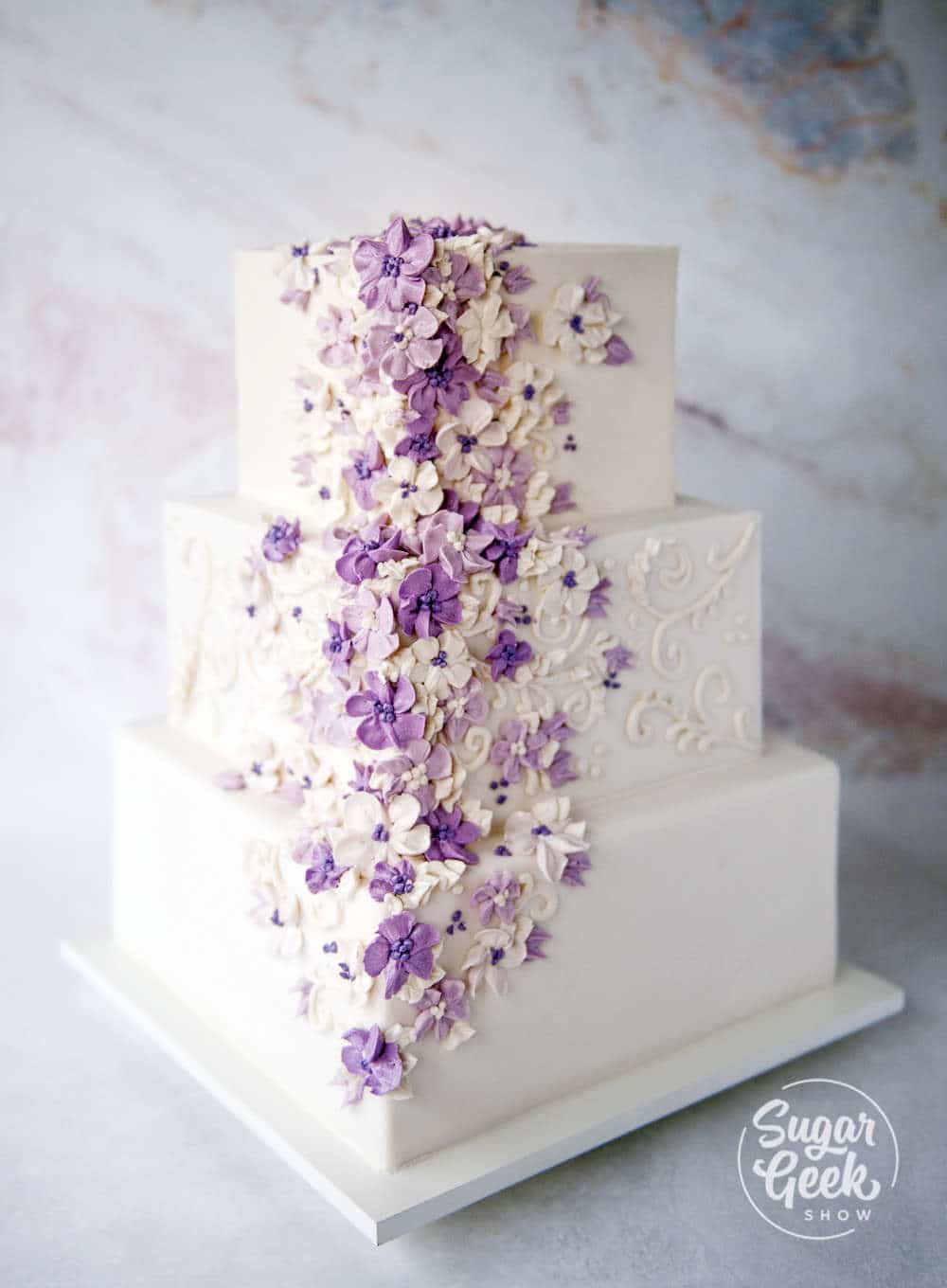 Three tier square white buttercream cake with purple buttercream flowers