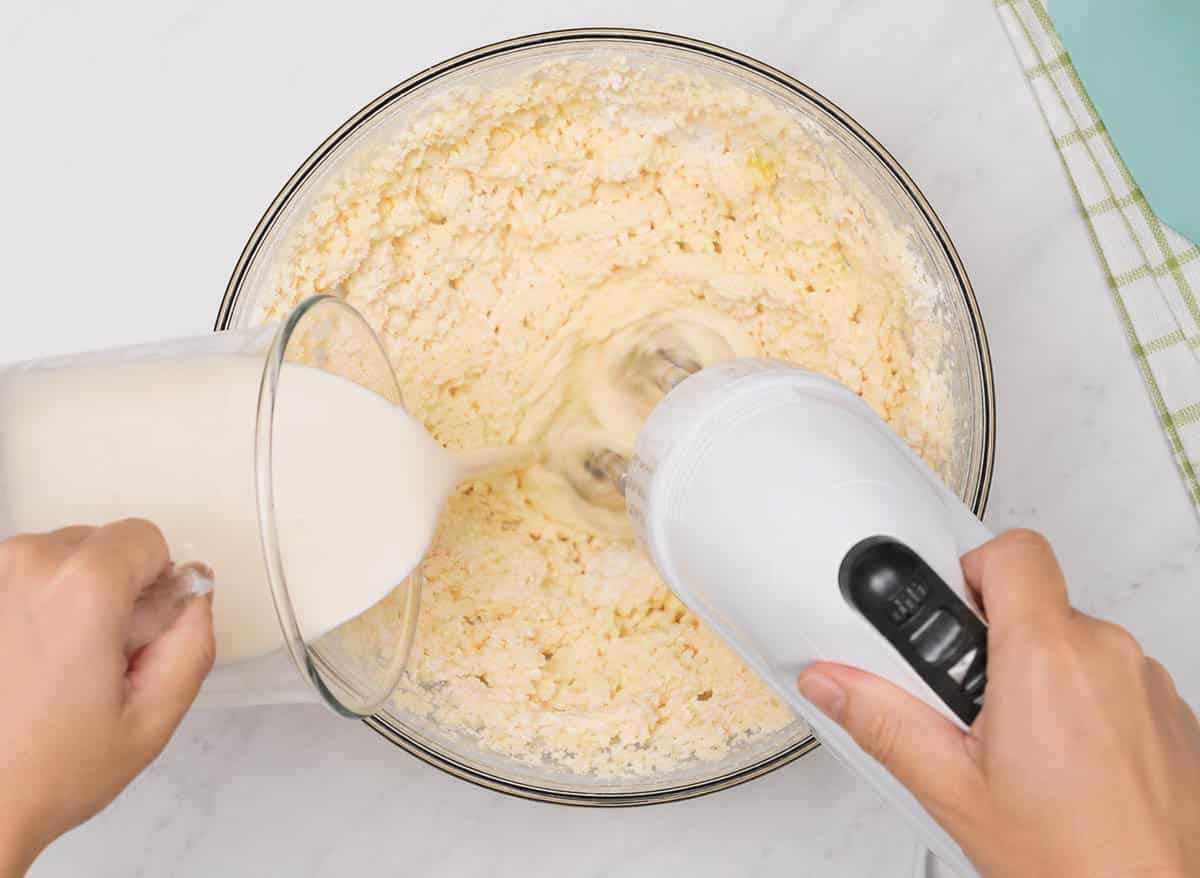 Adding cream into muffin batter with a hand mixer in a glass bowl.