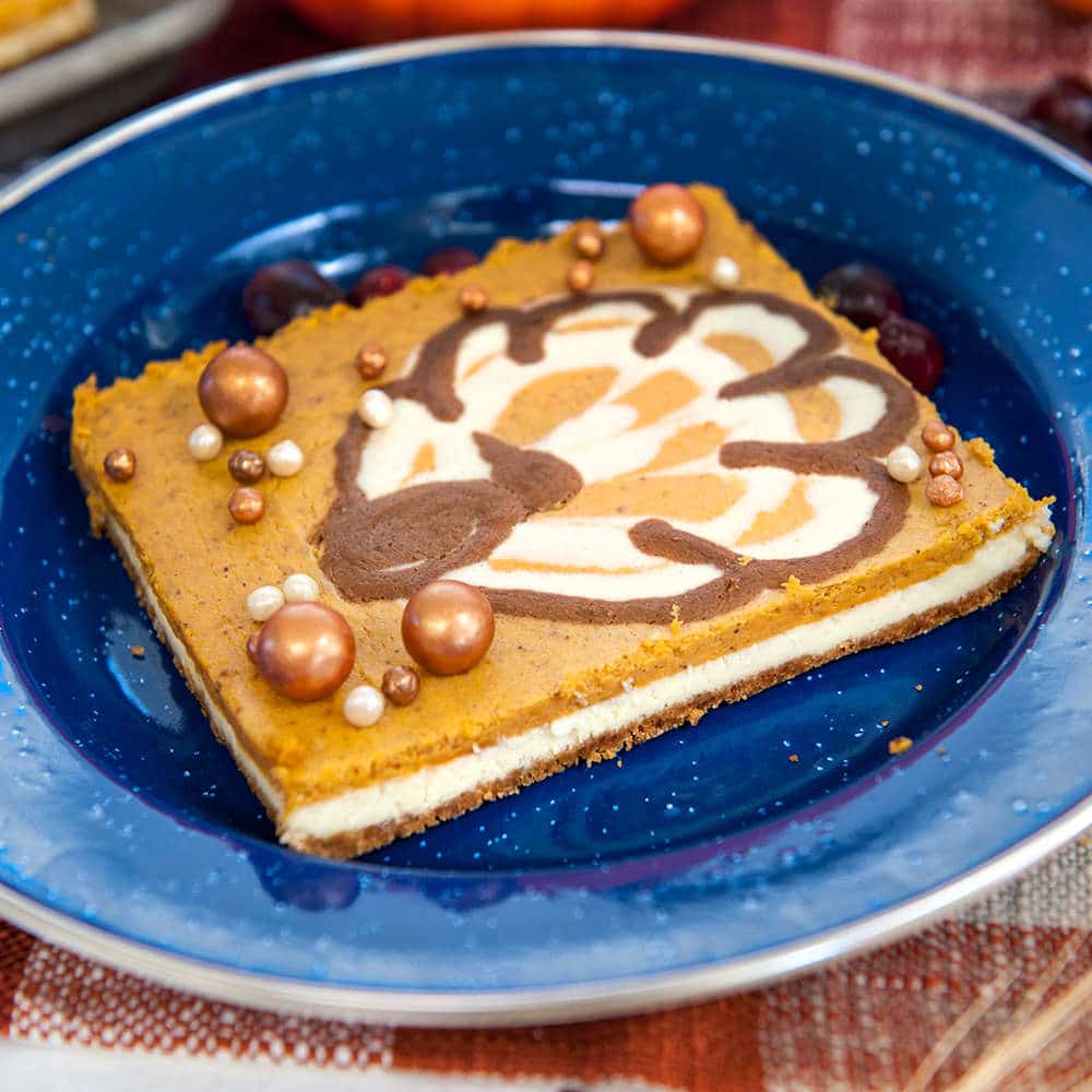 pumpkin cheesecake bars with turkey piped on top on blue plate
