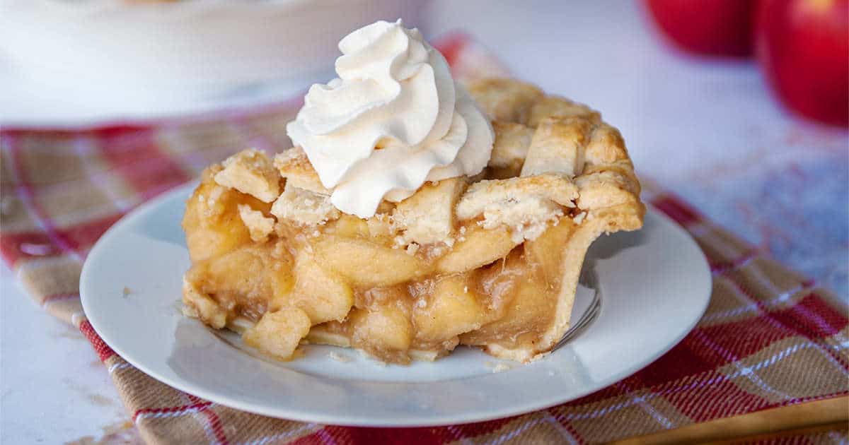 close-up of apple pie with lattice crust and whipped cream dollop on a blue plate