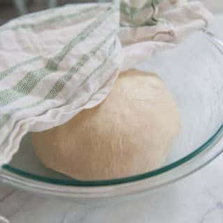 putting bread dough in a lightly greased bowl and covering with a towel to proof