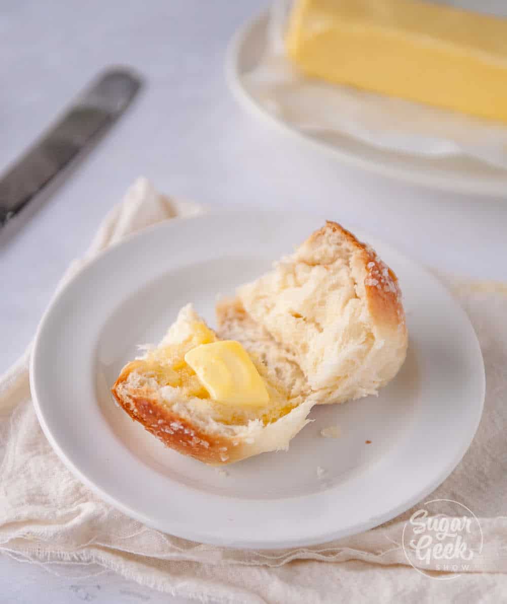 homemade dinner roll split open on a floral plate with pat of butter on top