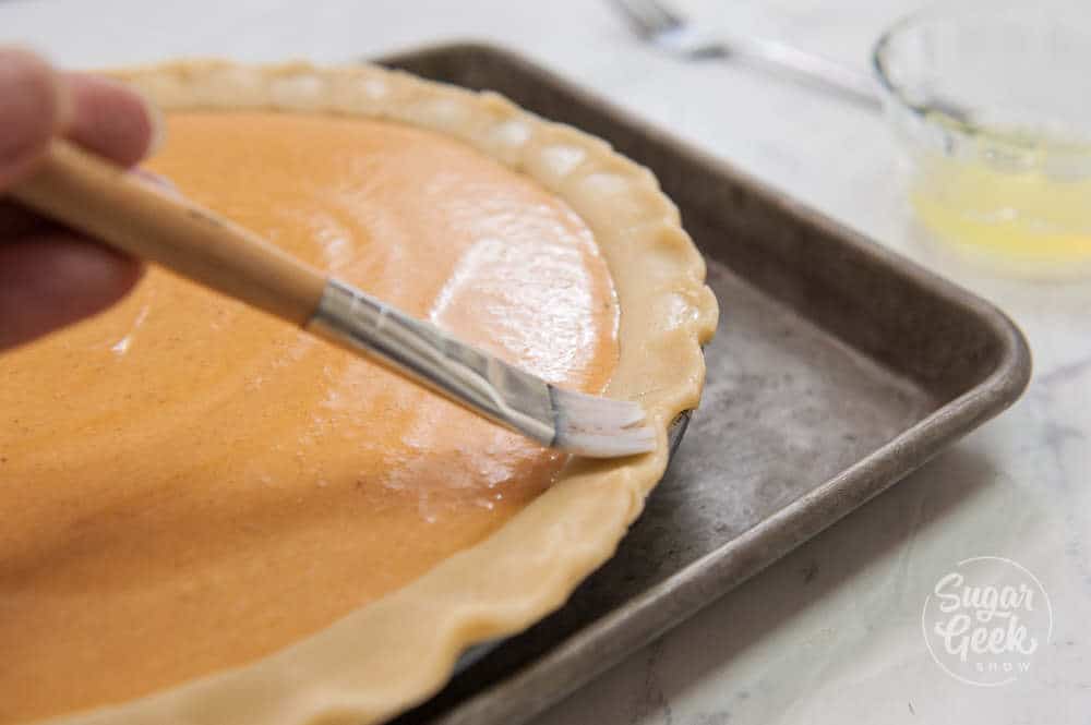 Pumpkin pie filled but not baked yet with the crust edges being brushed with an egg wash.