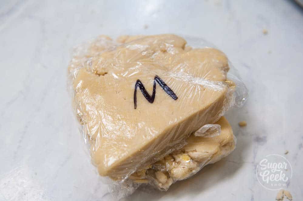 Mealy pie dough wrapped in plastic wrap to chill and labeled with an "M."