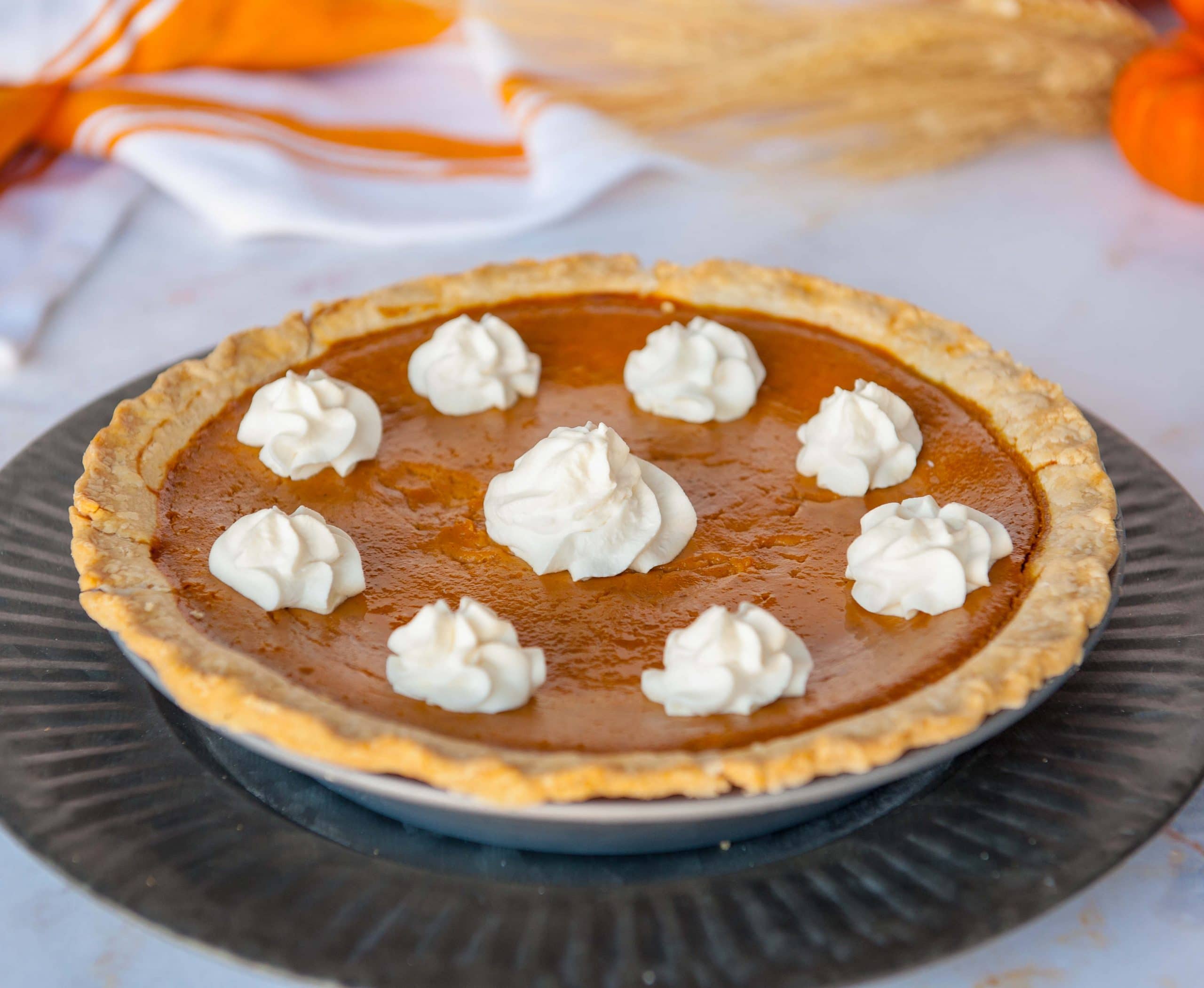 close-up of pumpkin pie on black plate with whip cream dollops on top