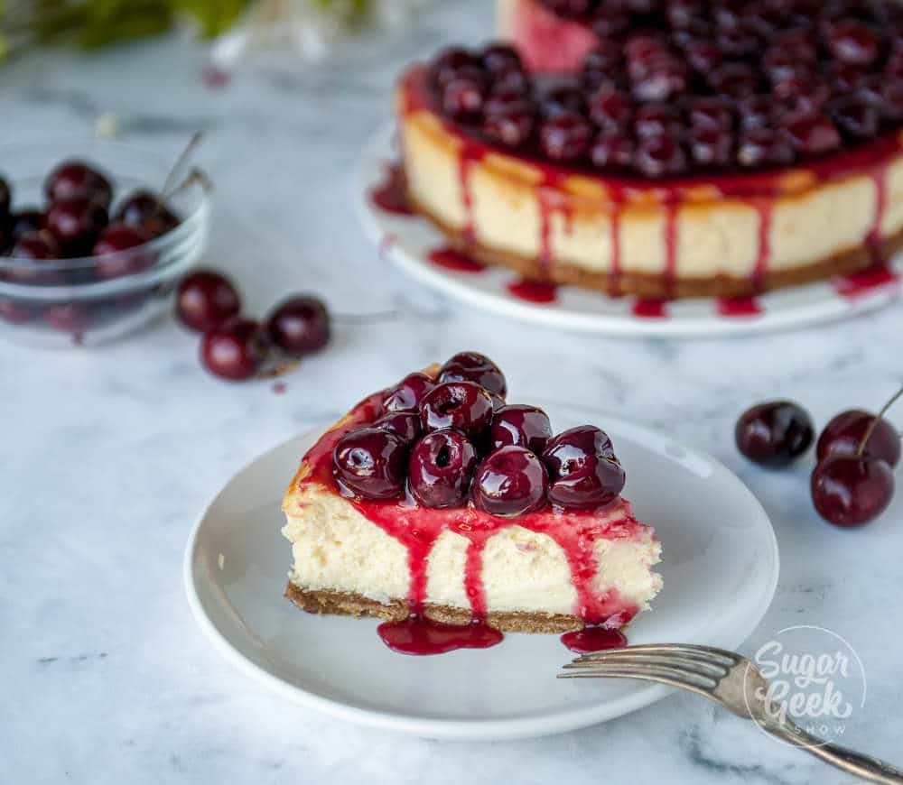 slice of cherry cheesecake on a white plate with cheesecake in the background