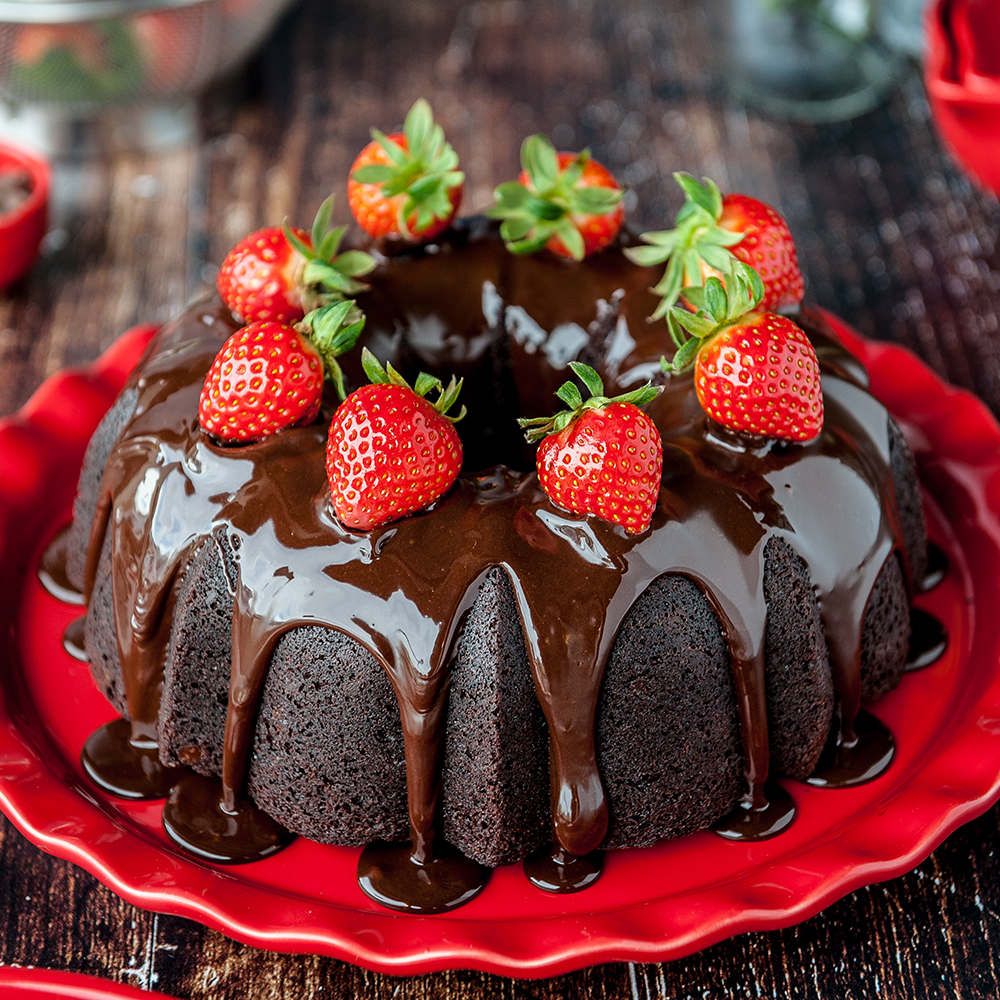 chocolate bundt cake with chocolate ganache and strawberries on a red plate