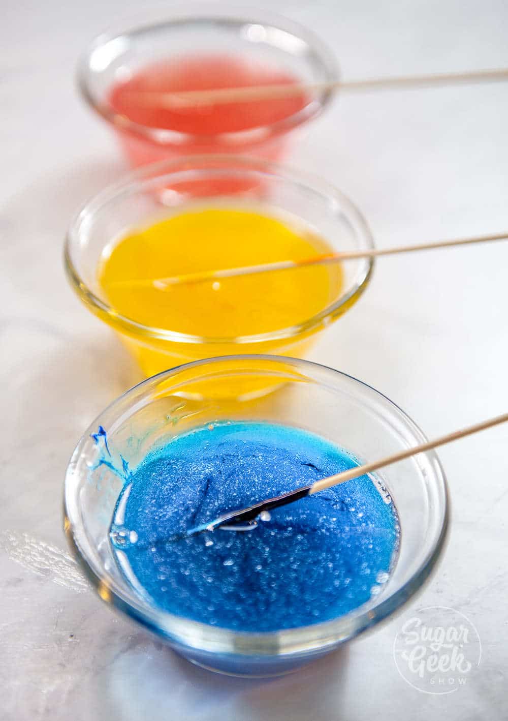 gummy bear mixture divided into three bowls with coloring and flavoring added