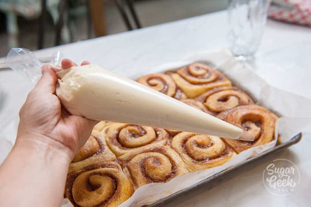 adding frosting to cinnamon rolls