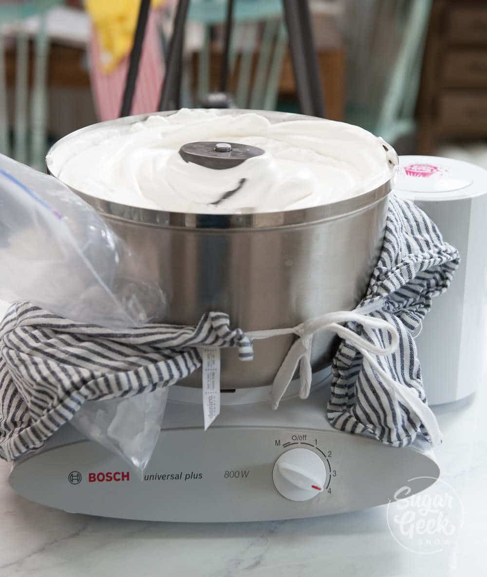 Metal mixer whipping Italian meringue with ice and towels wrapped around the base.