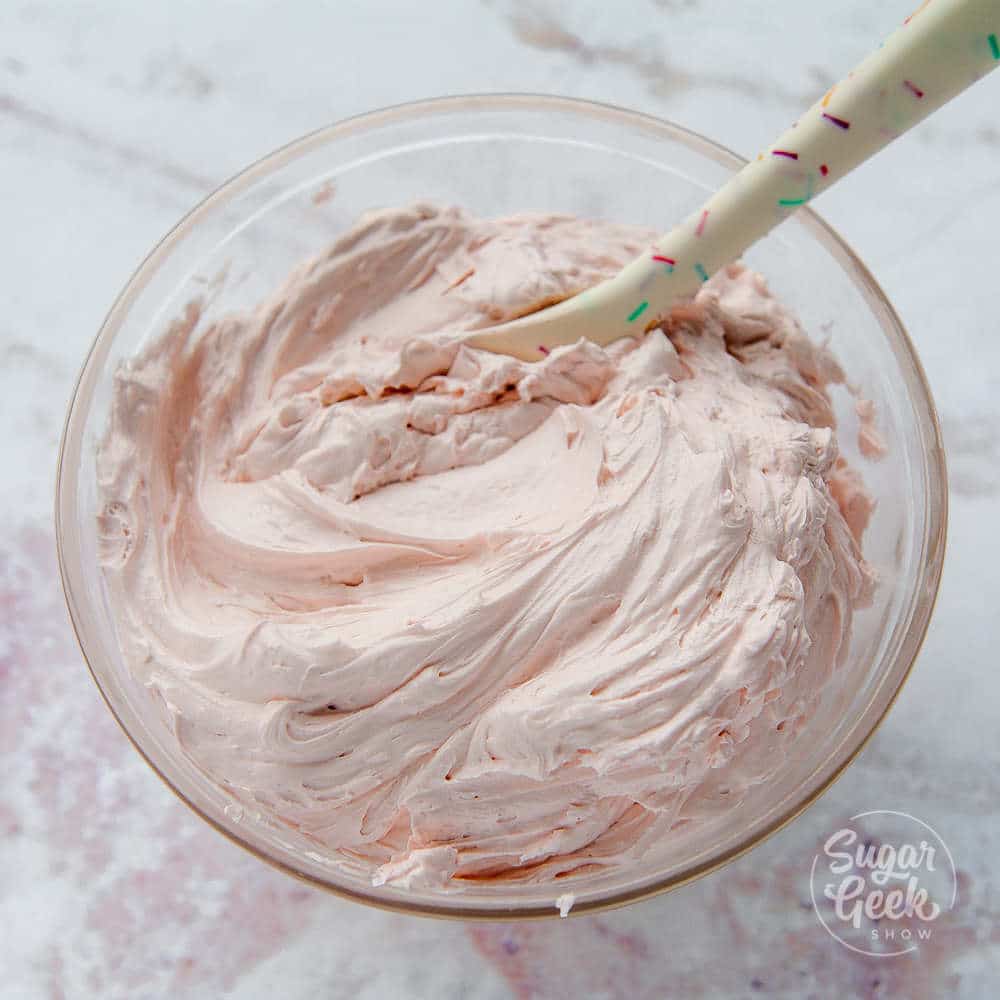 italian meringue buttercream colored light pink in a bowl with a spatula