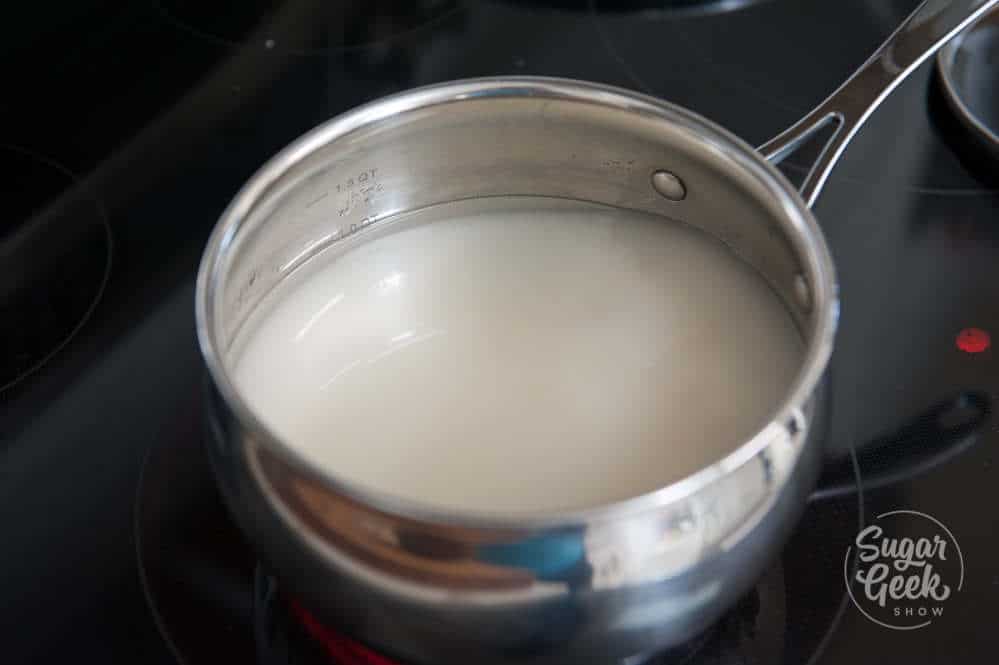 Close up of metal saucepan with water and sugar on a stovetop.